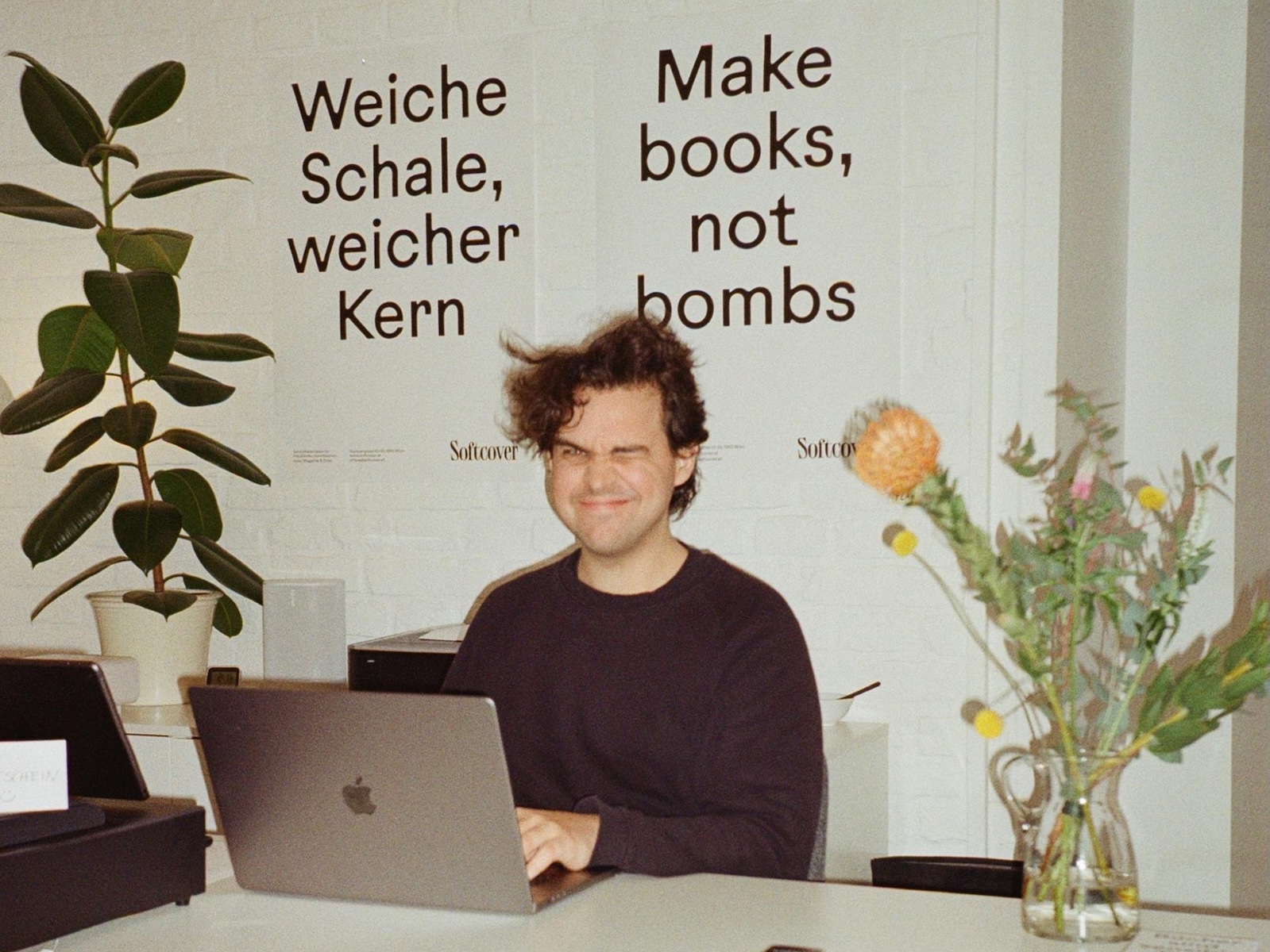 Softcover founder Sebastian Gansrigler at the counter beneath posters reading 