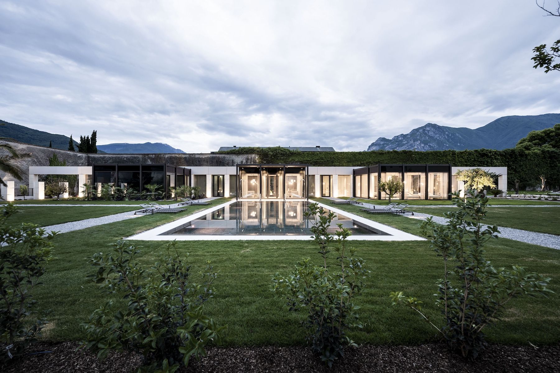 Hotel Arx Vivendi | Walled-garden wellness hotel at dusk with a long reflecting pool and Dolomite peaks beyond, near Lake Garda