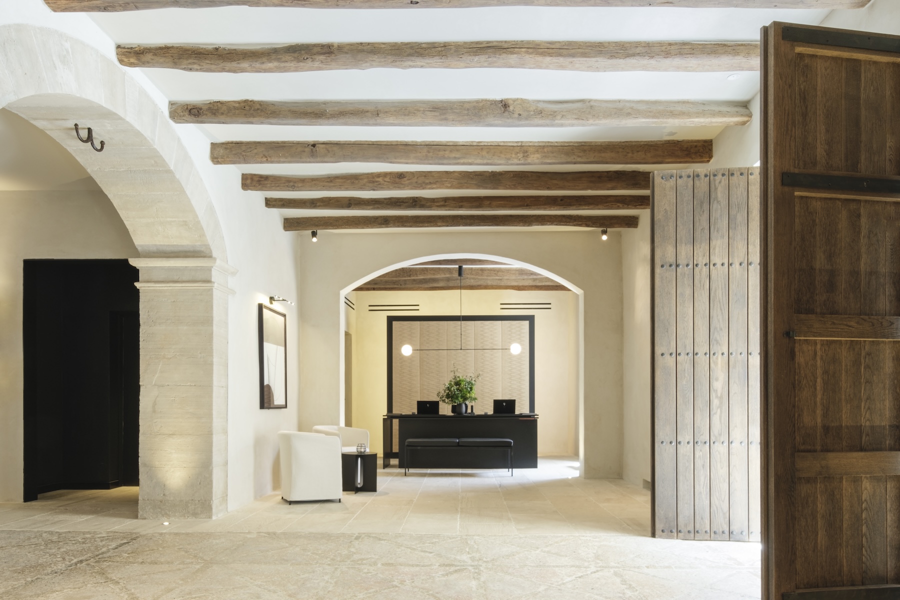 Reception at Can Ferrereta framed by a stone arch, exposed timber beams and a studded oak door | The Aficionados