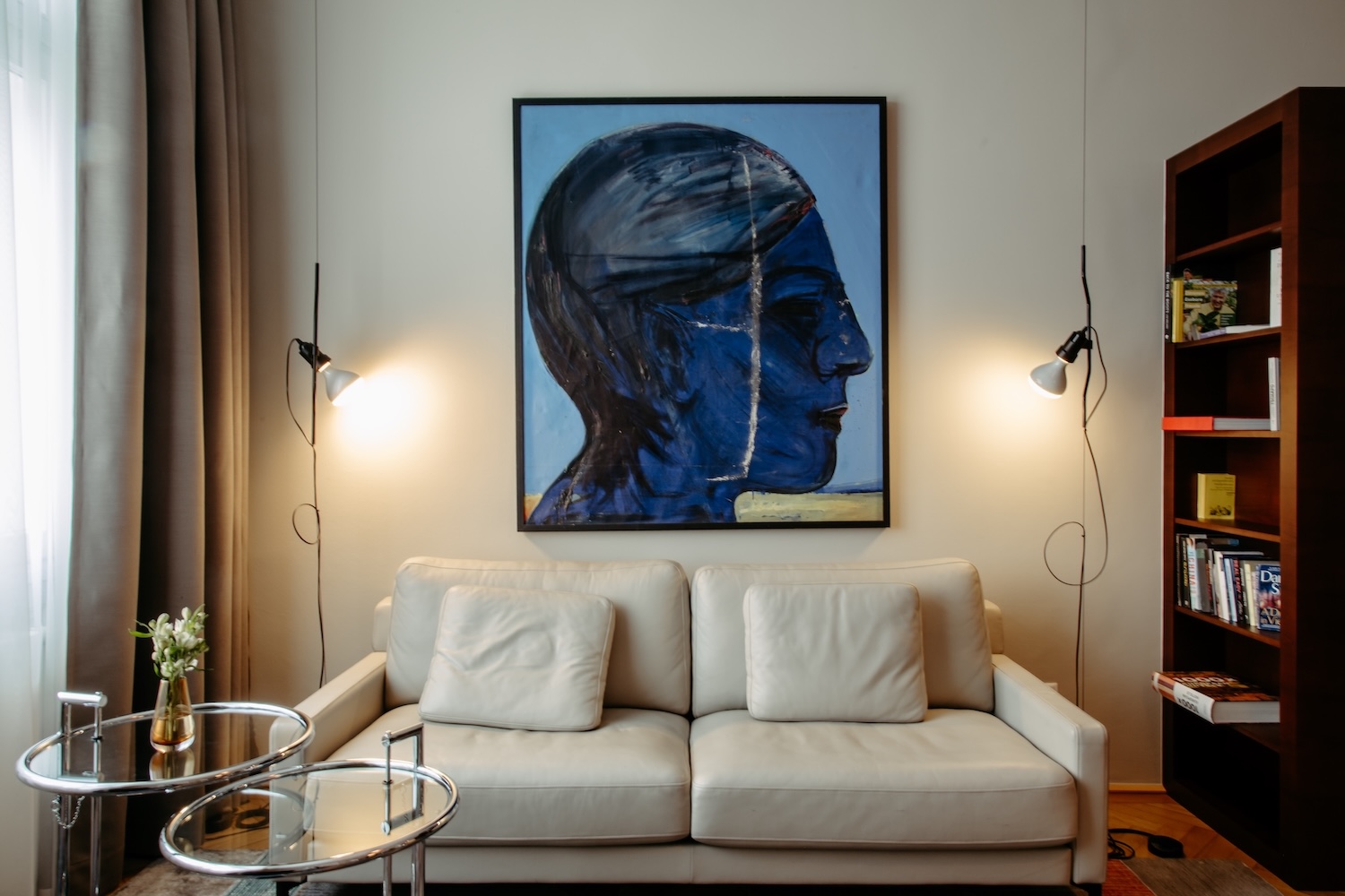 A large blue portrait above the pale leather sofa in the sitting room of the Harry K Room at Hotel Altstadt Vienna, with one of Eileen Gray's glass tables in the foreground | The Aficionados.