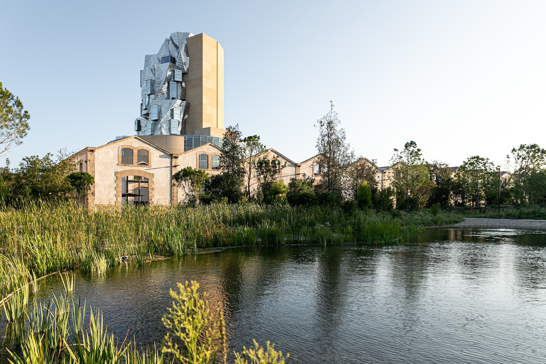 Frank Gehry's mirrored LUMA tower rising above the restored stone ateliers and reed-fringed wetland gardens of Parc des Ateliers, Arles | The Aficionados