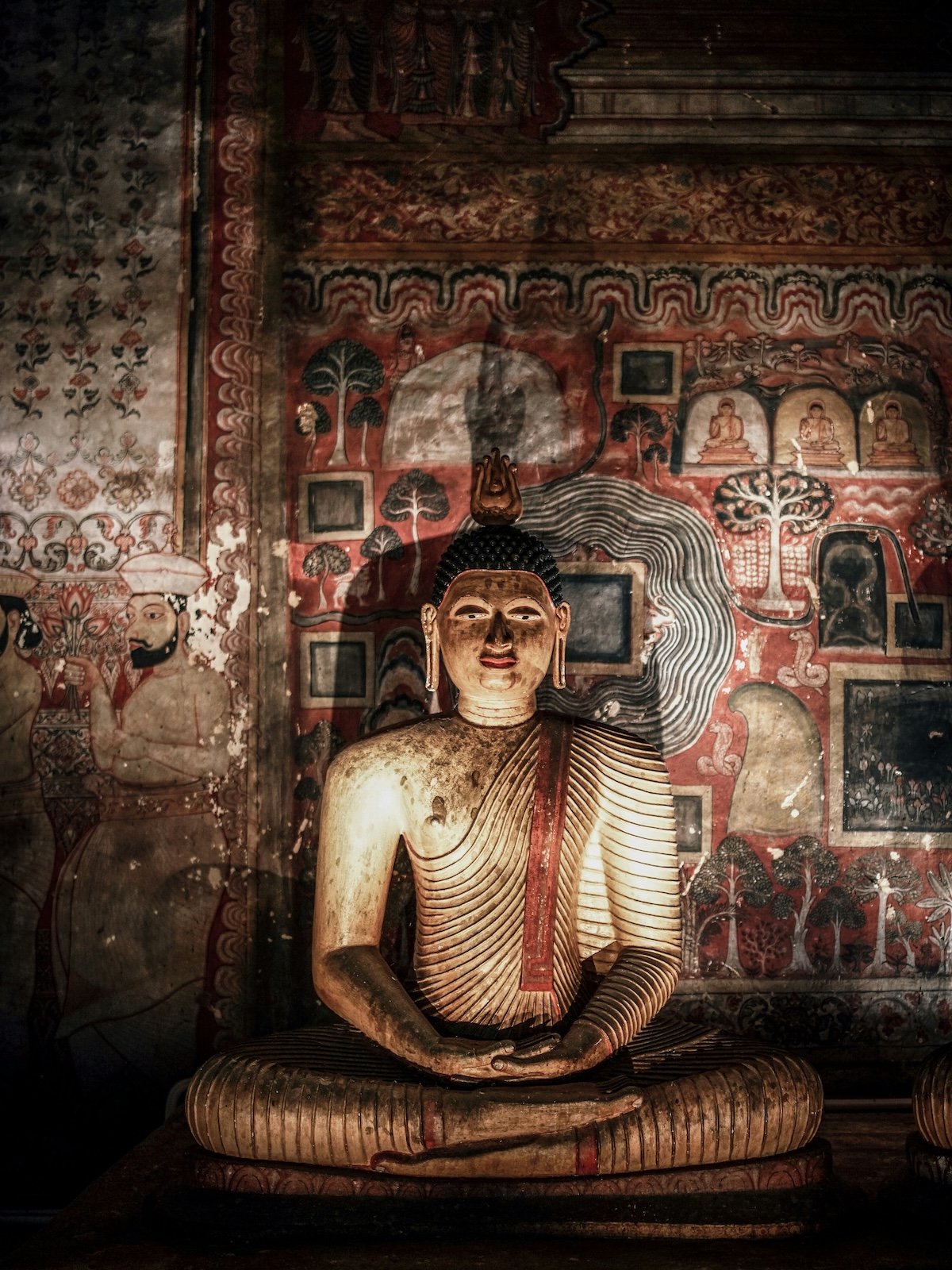 Gilded seated Buddha against painted murals inside the cave temples at Dambulla, Cultural Triangle, Sri Lanka | The Aficionados