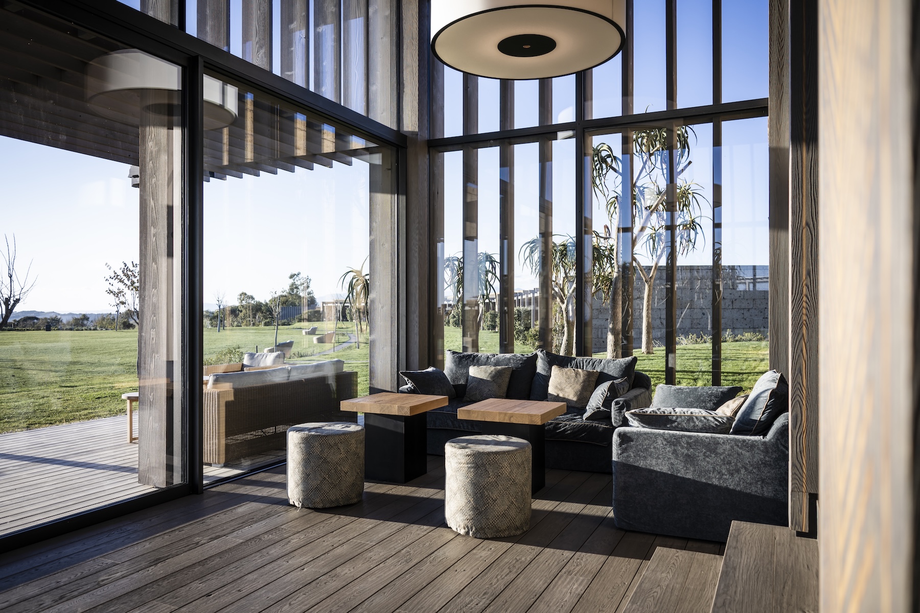 Double-height lounge at ADLER Spa Resort Sicilia with timber-slatted glazing, velvet sofas and views onto the garden | The Aficionados