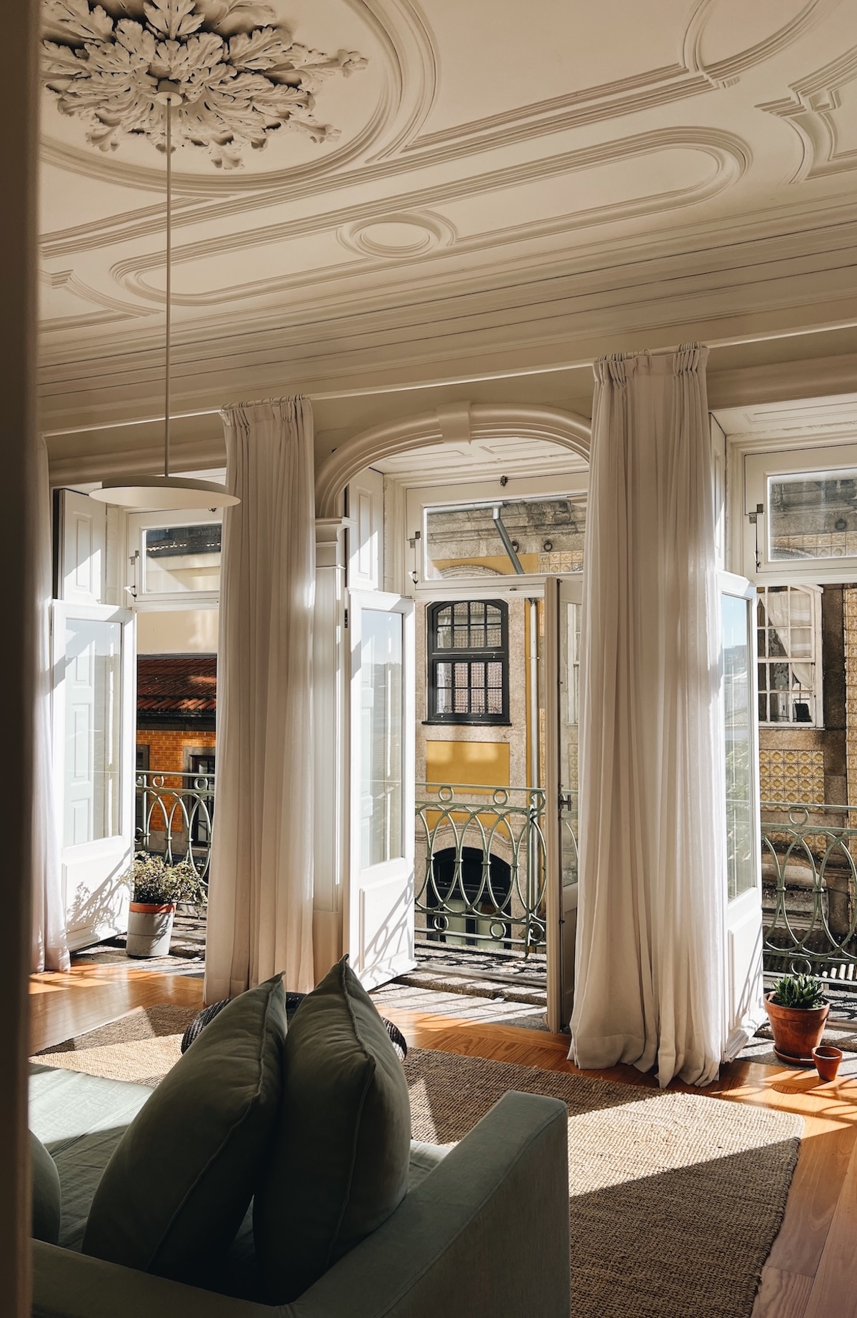 A sunlit white apartment at B28 Apartments, Porto, Portugal, its shuttered doors opening onto a balcony above the city's terracotta rooftops and the river beyond.