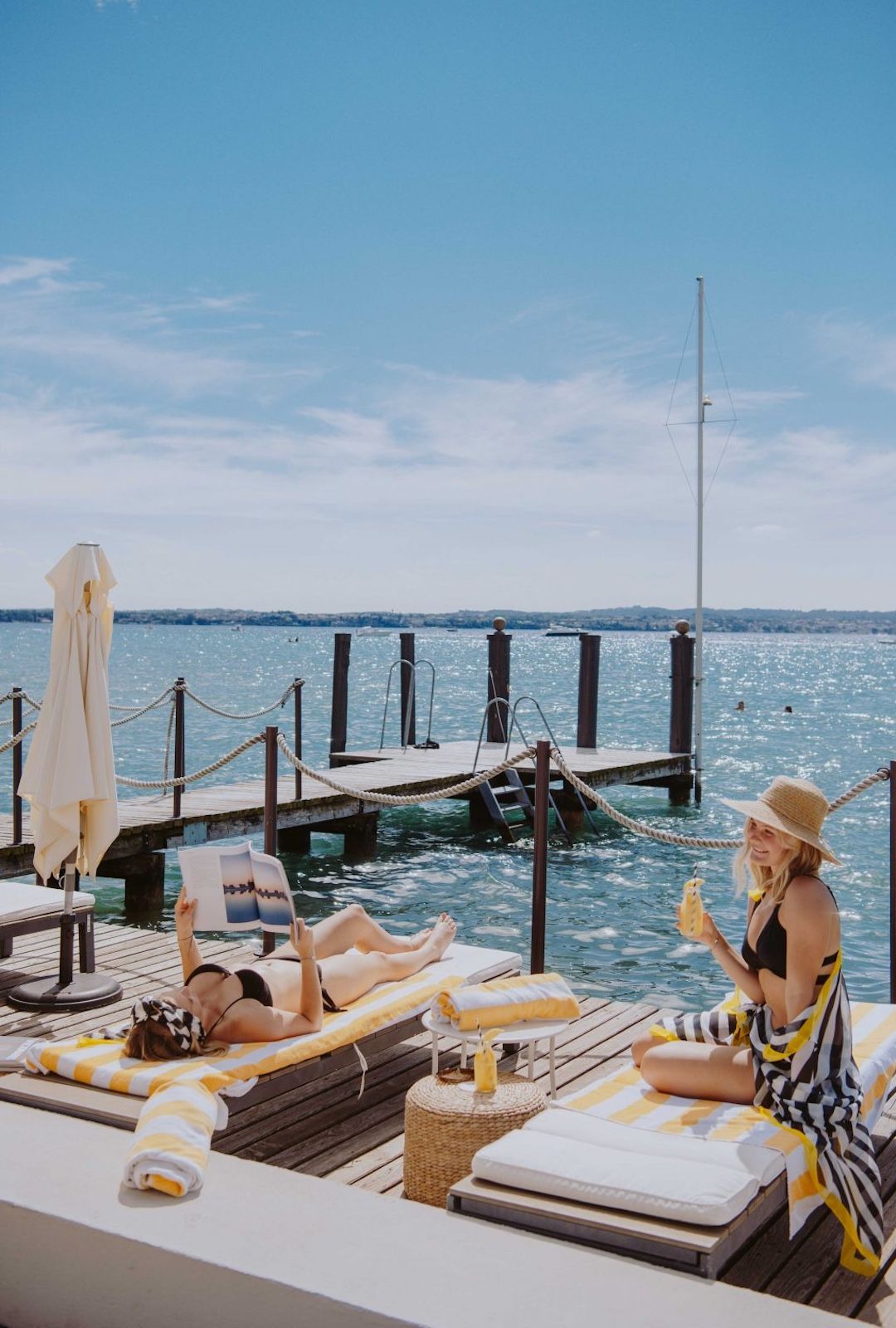 AQVA Boutique Hotel private getty | Two women sunbathing on striped loungers at a lakeside lido jetty on Lake Garda