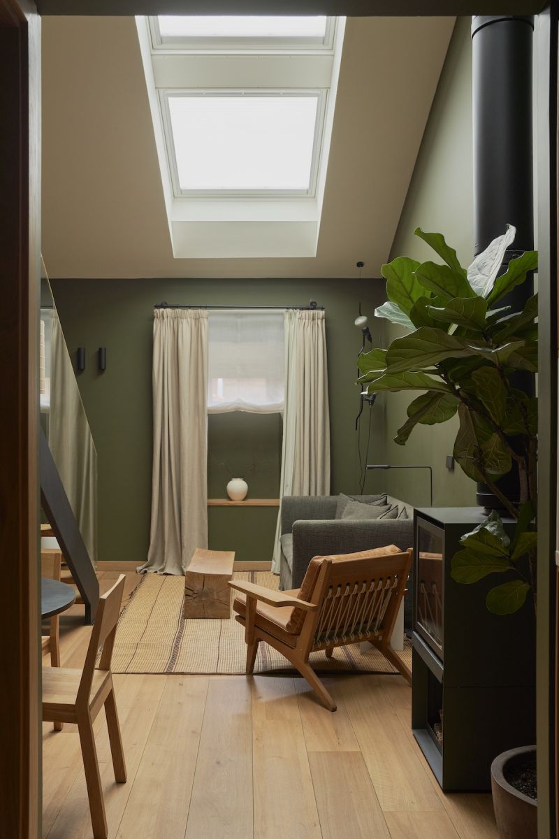 Attic suite at Hotel Arbaso with skylights, oak lounge chair and wood-burning stove against forest-green walls | The Aficionados
