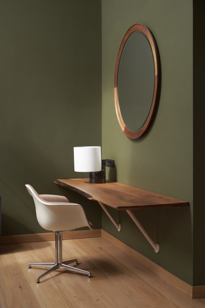 Forest-green guest room corner at Hotel Arbaso with a live-edge walnut desk, oval mirror and Eames chair | The Aficionados