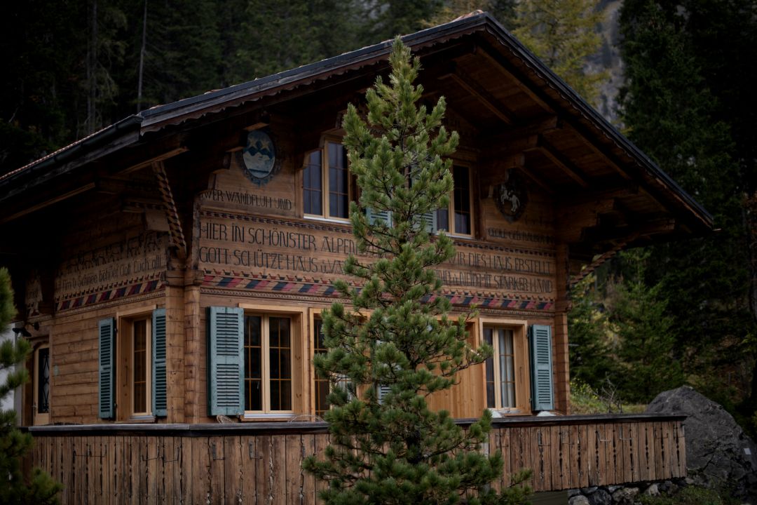 Timber Chalet Arva above Kandersteg, carved Alpine inscriptions on the gable and blue-green shutters framed by pines.