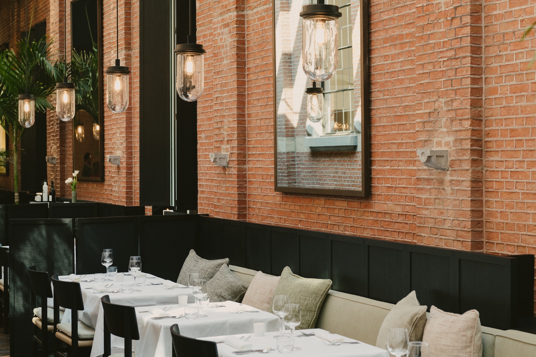 Brick-walled dining room with black banquette seating, white-clothed tables and glass pendant lights at August, Antwerp | The Aficionados