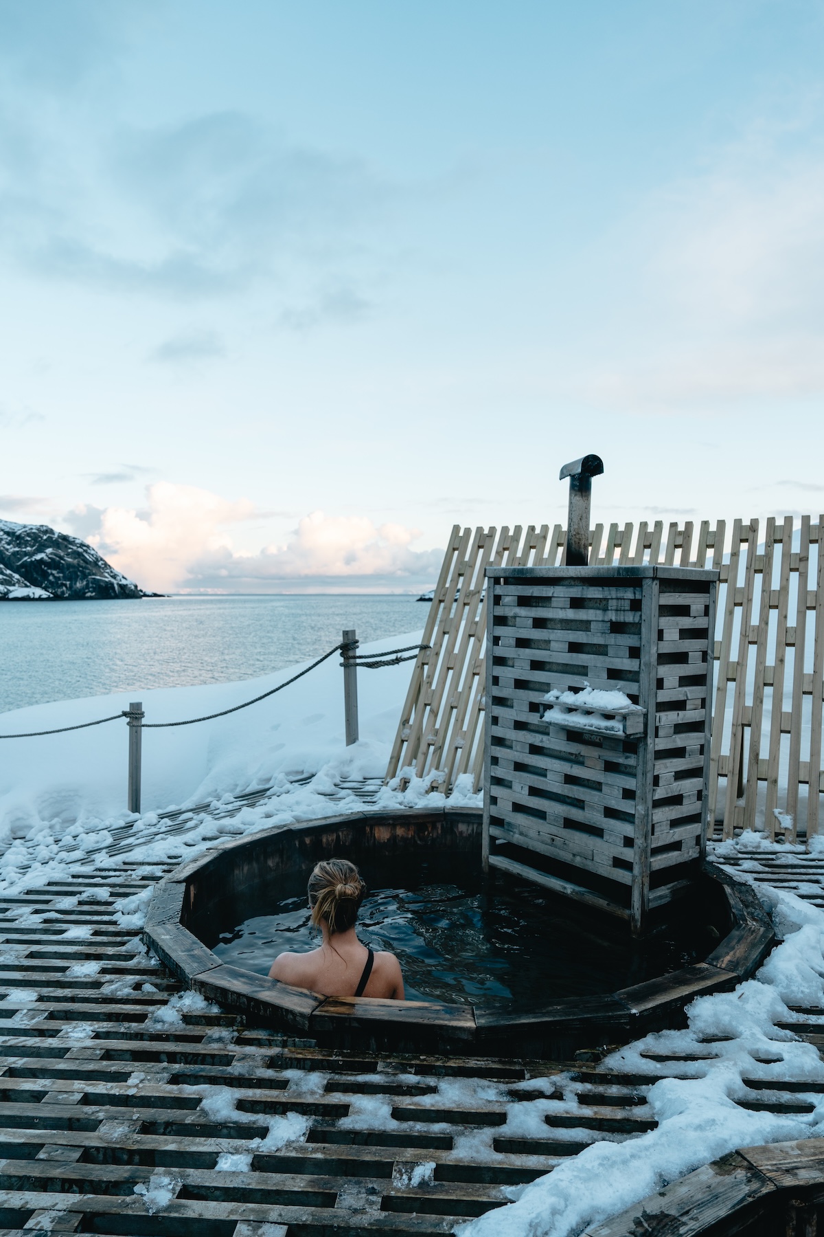 A wood-fired hot tub in the snow at Nusfjord Arctic Wellness, Lofoten, looking out to a calm winter sea | The Aficionados
