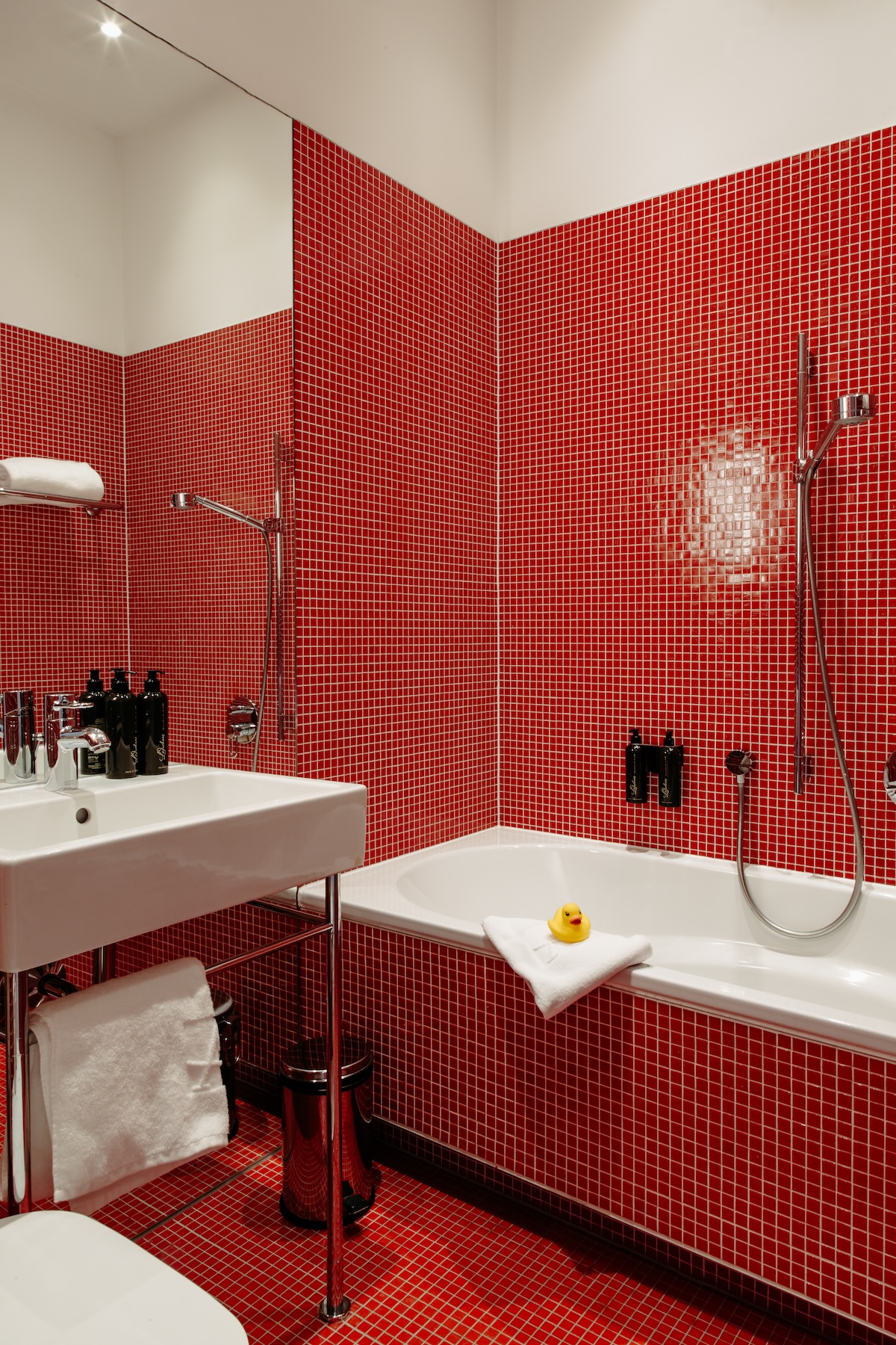 A yellow rubber duck on a folded towel beside the bath, in the red mosaic-tiled bathroom of the Harry K Room at Hotel Altstadt Vienna | The Aficionados.