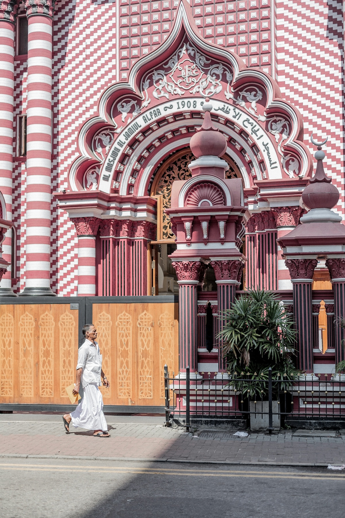 A man in a white sarong walks past the striped 1908 façade of the Jami-Ul-Alfar Red Mosque in Pettah, Colombo