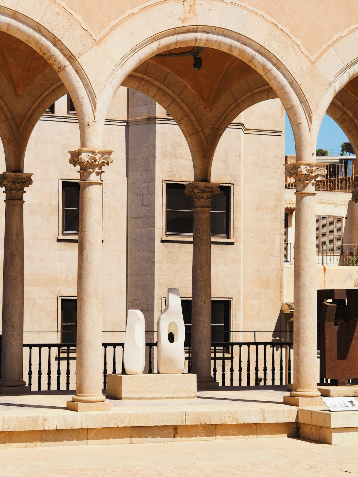 White abstract sculptures on the arcaded terrace at Palau March, framed by Gothic columns above the cathedral steps | The Aficionados
