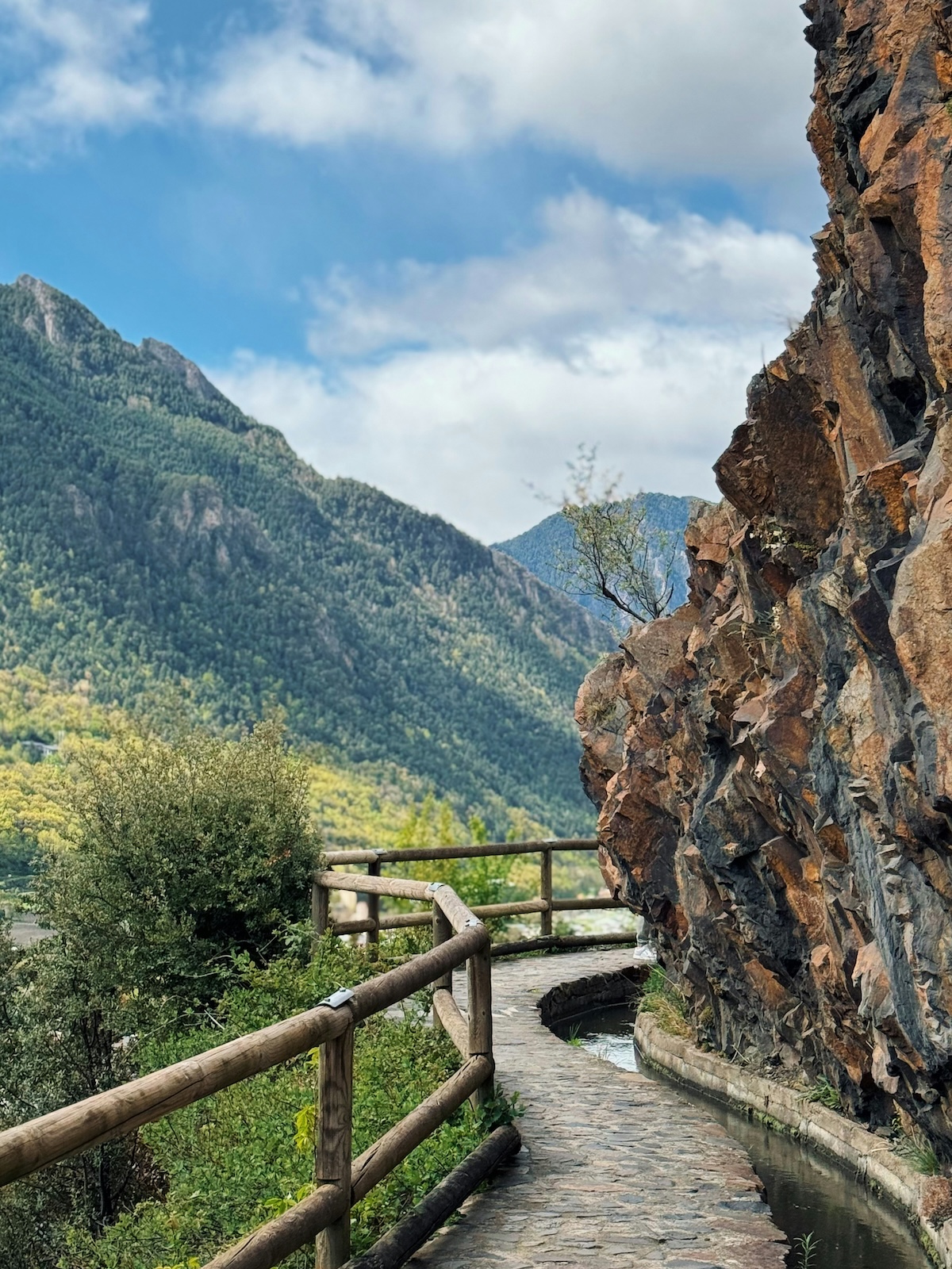 Wooded ridge and rock summit seen from a railed walking path in the Valira valley, Andorra