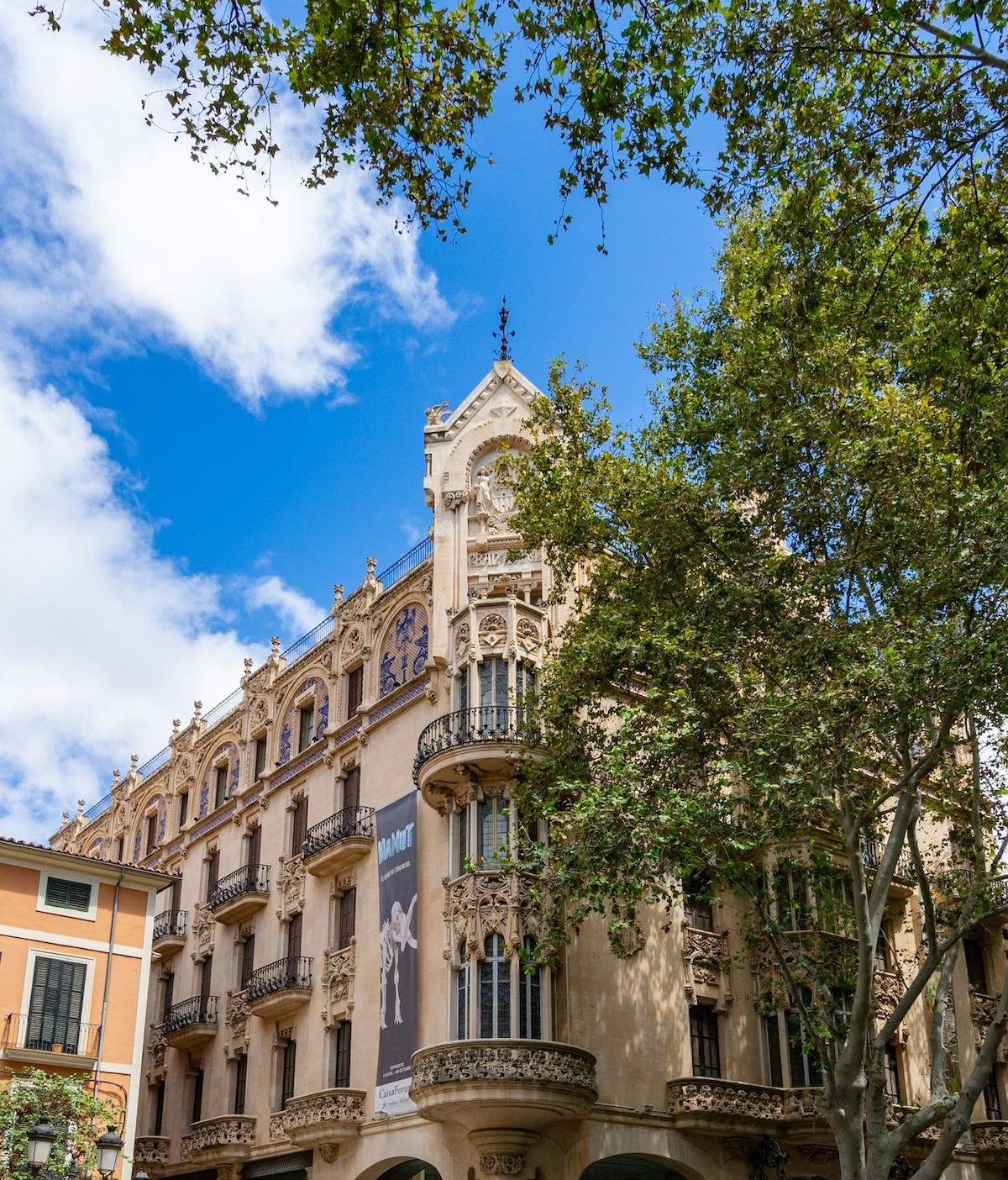 The carved Modernisme façade of the Gran Hotel on Plaça Weyler, now CaixaForum, seen through plane trees | The Aficionados