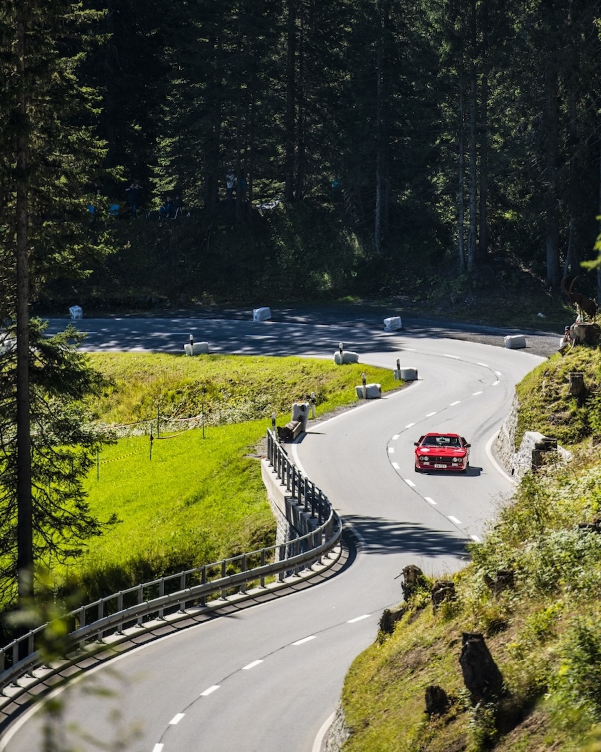Red classic coupe descending a winding forest road on the Langwies to Arosa hillclimb | The Aficionados