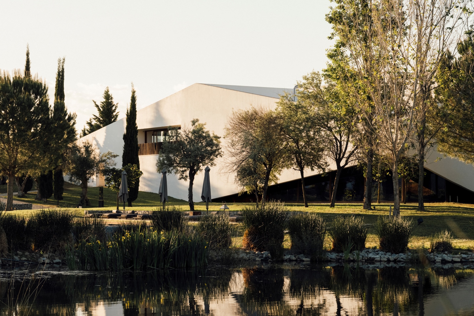 L'AND Vineyards, Montemor-o-Novo, Alentejo: angular whitewashed hotel by Márcio Kogan (Studio MK27) mirrored in the estate lake at golden hour.