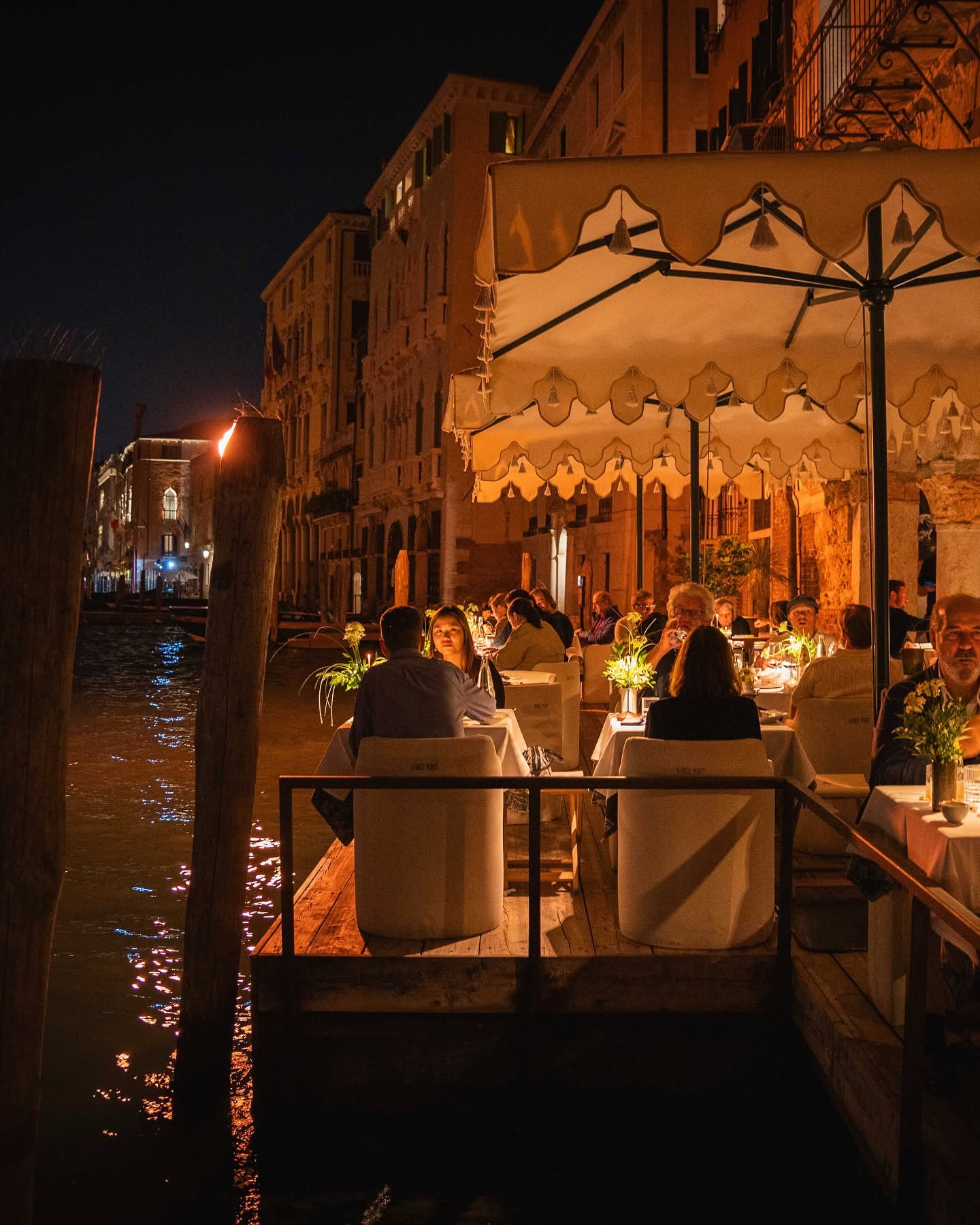 Diners at Francy's candlelit Grand Canal terrace at night, under a scalloped white umbrella beside the water in Venice.
