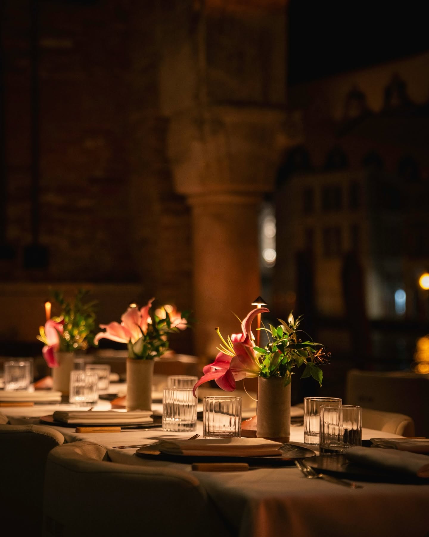 Table setting at Francy's with pink lilies, candlelight and ribbed glassware against a Byzantine stone column.