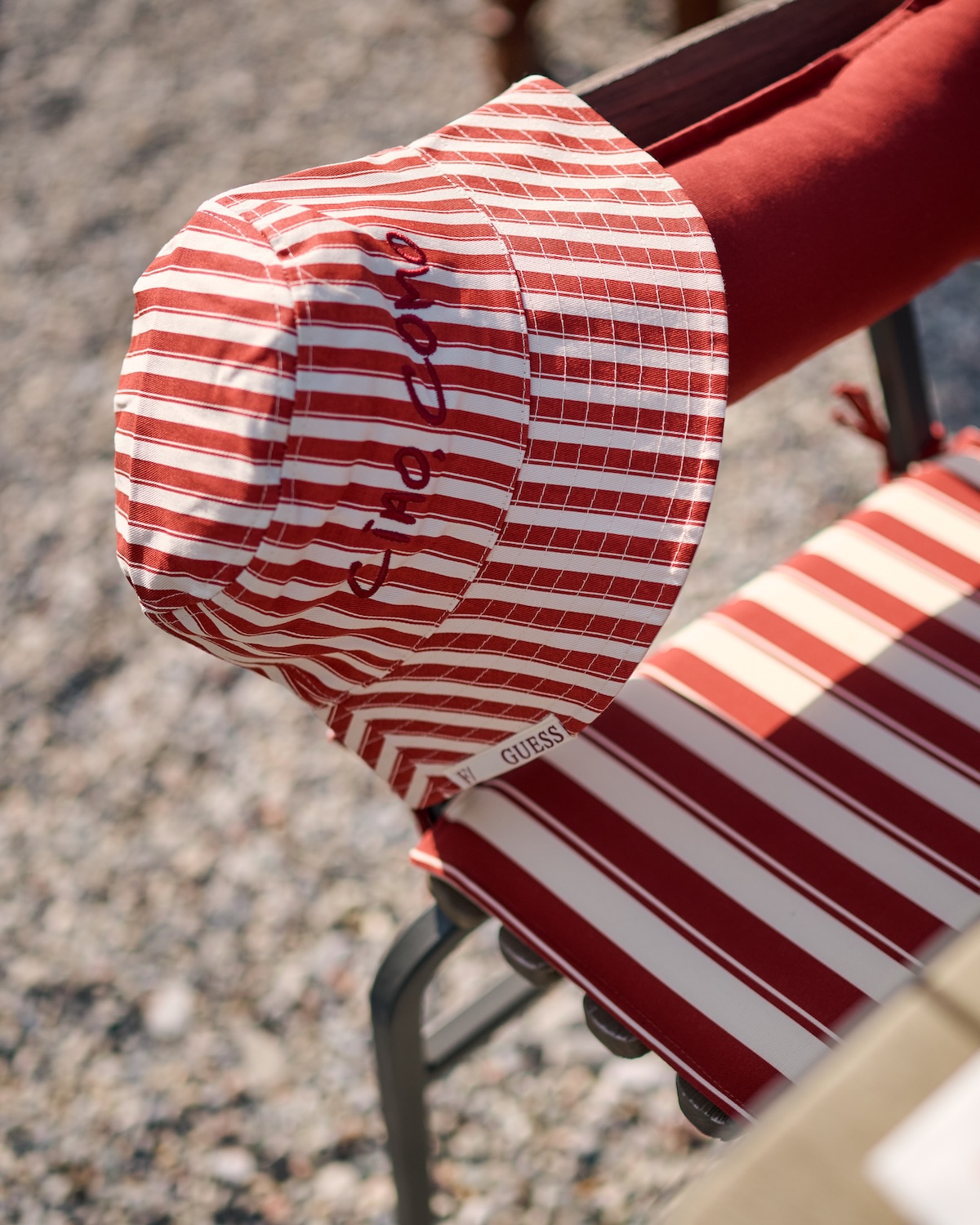Ciao Como embroidered detail on red-and-cream awning stripe textile, GUESS x Filario lido accessory, Made-in-Como fabric, summer 2026 collaboration | TheAficionados.com