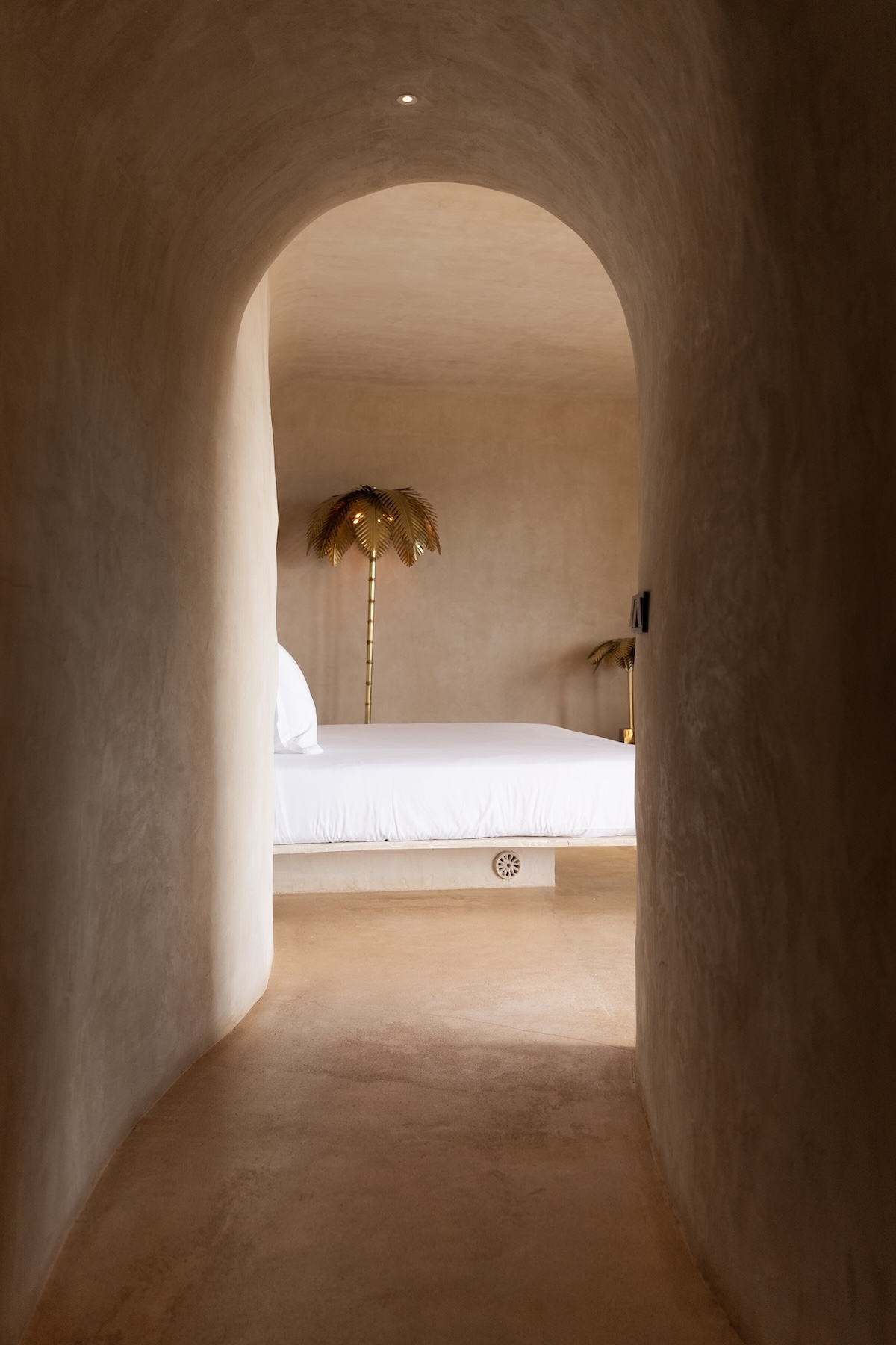 Curved plaster bedroom at Hannah Formentera with a platform bed and brass palm-tree lamps | The Aficionados