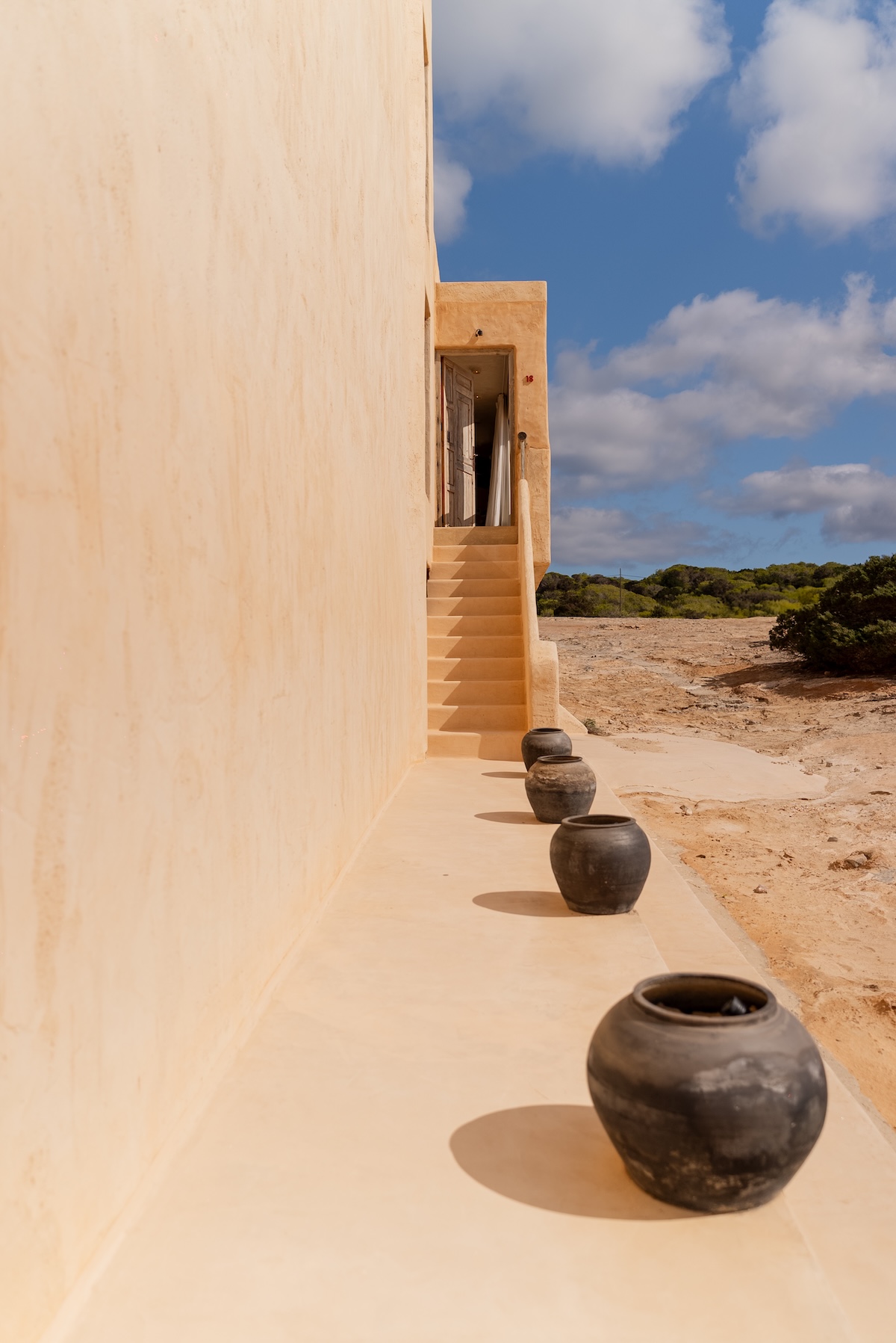 Sand-coloured plaster exterior at Hannah Formentera with a stone staircase and dark clay pots on the Migjorn dunes | The Aficionados