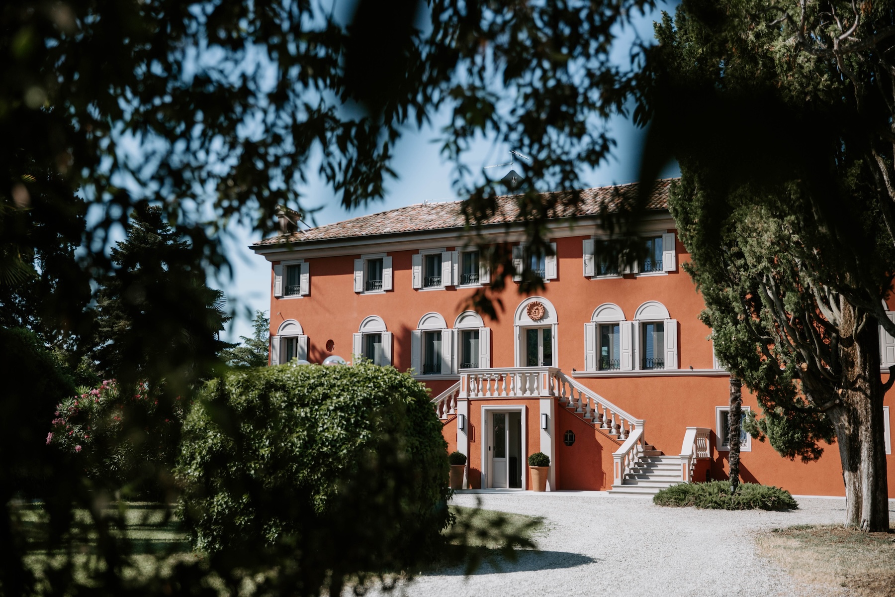 Terracotta-hued Villa Manodori with a double balustrade staircase, glimpsed through the trees on the Venturini Baldini wine estate