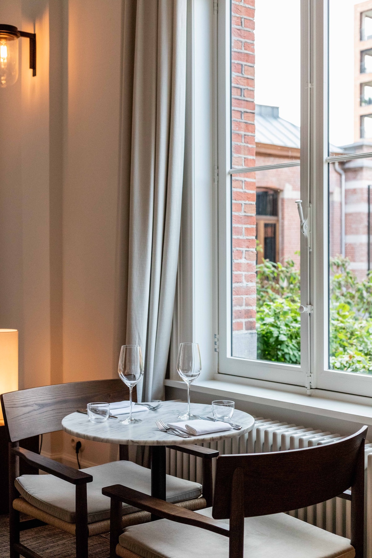 Marble corner table with wine glasses beside a window onto the gardens at August, Antwerp | The Aficionados