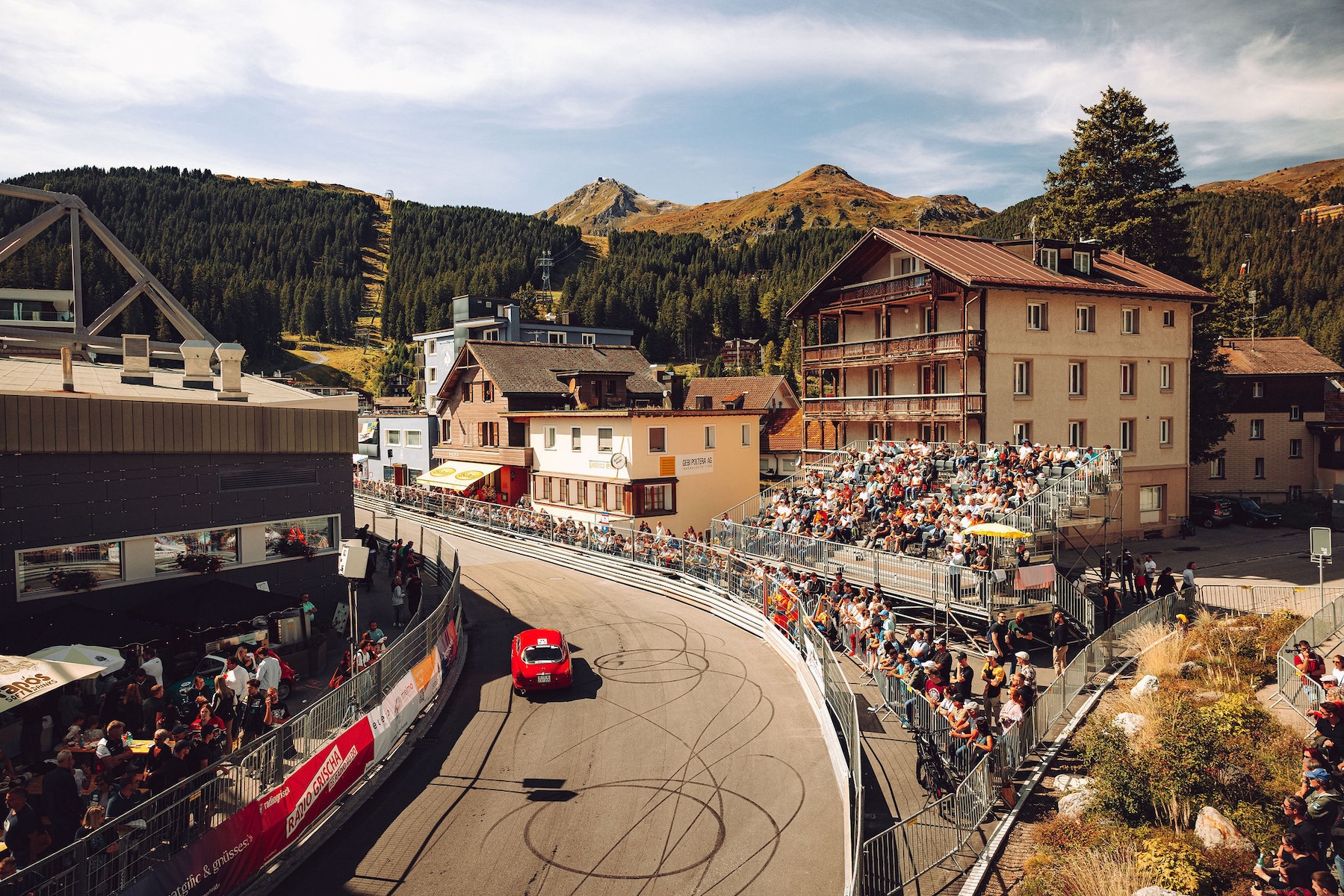 Spectators packing the grandstand as a red car corners the town section through Arosa village | The Aficionados