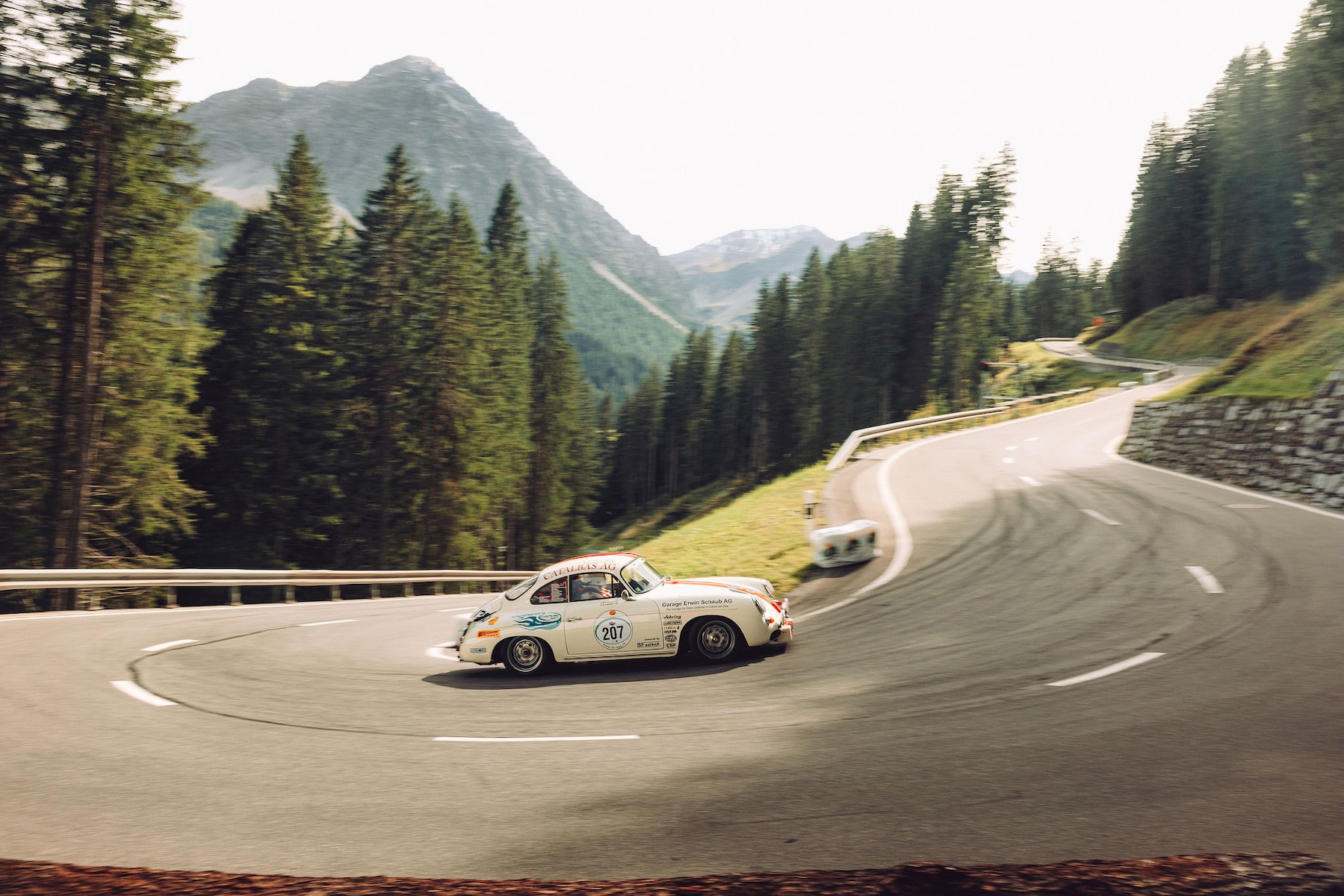 White Porsche 356 racing number 207 rounding a forested hairpin on the Arosa ClassicCar hillclimb | The Aficionados