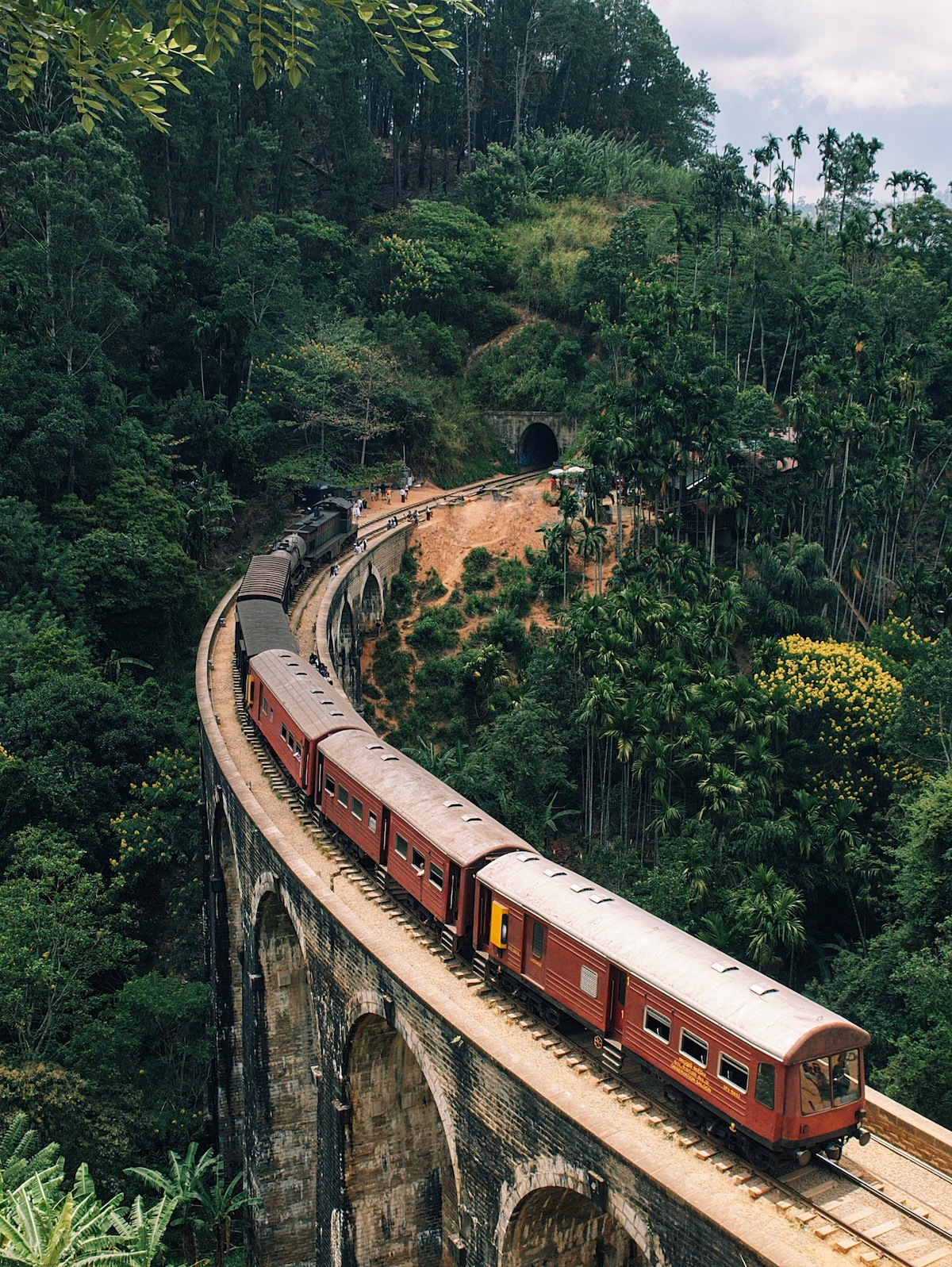 Red train crossing the Nine Arches Bridge through dense jungle near Demodara, tea country, Sri Lanka | The Aficionados