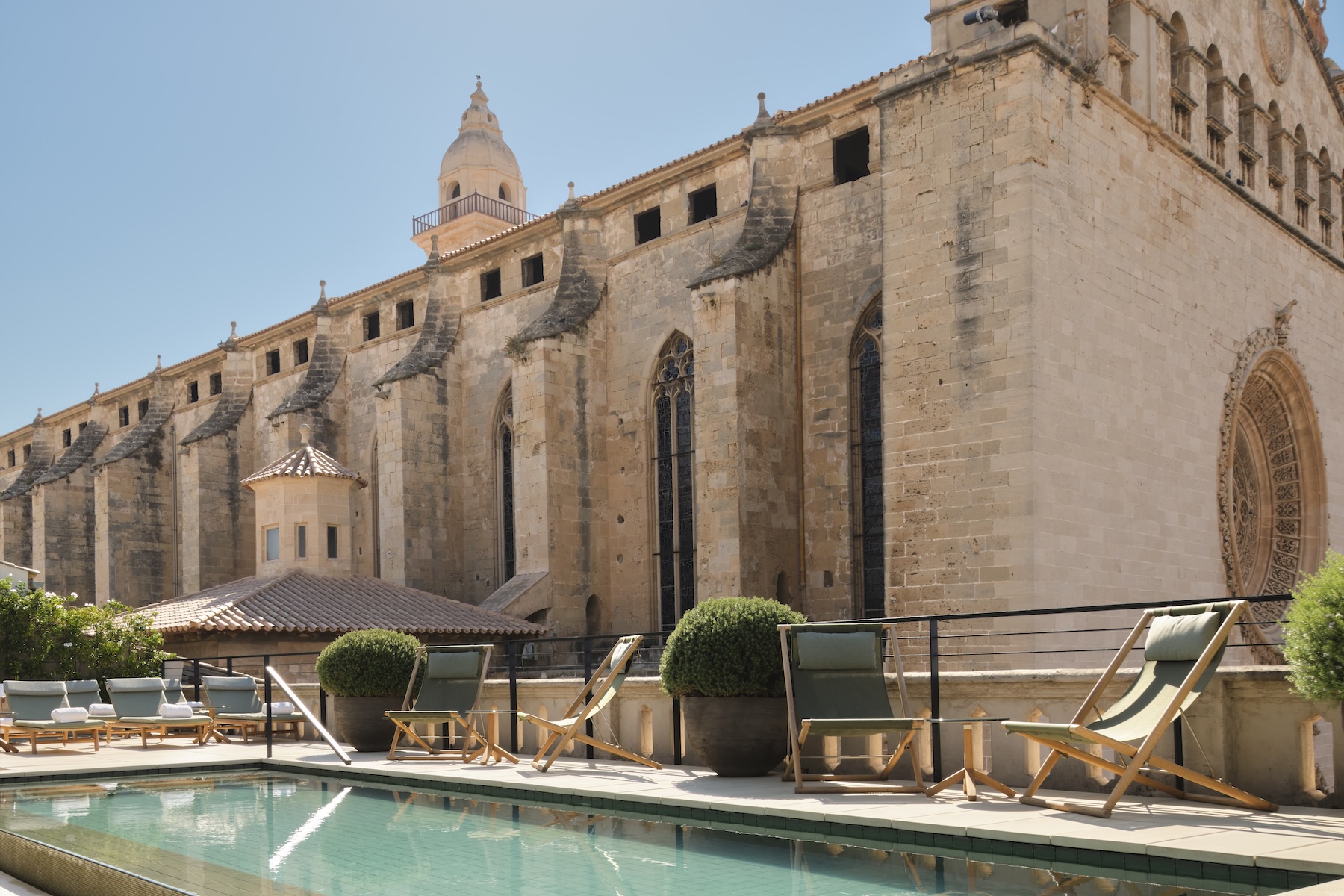 Rooftop pool and green deck chairs at Sant Francesc Hotel beside the Gothic flank and rose window of Sant Francesc basilica, Palma | The Aficionados