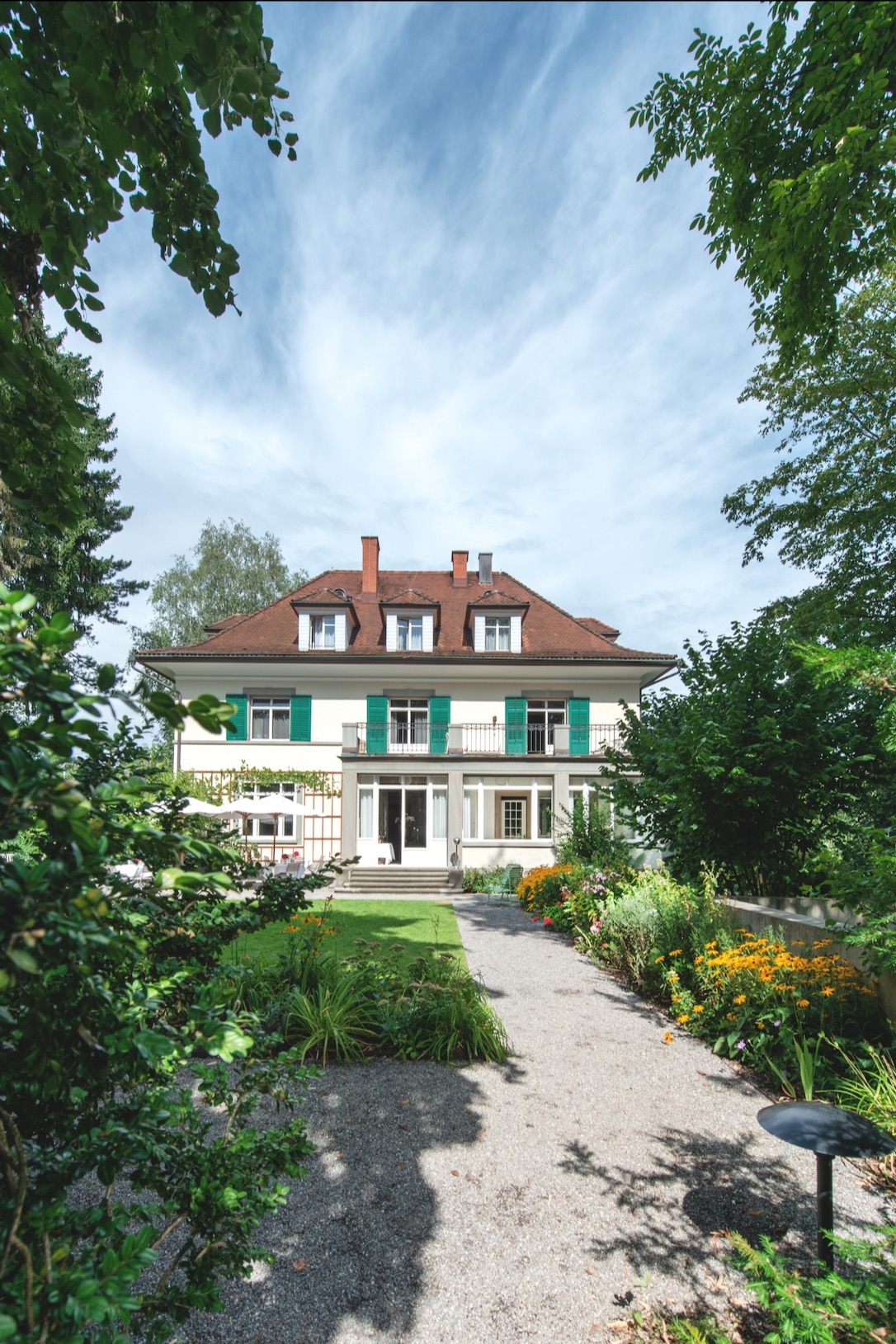 Signau House 1912 patrician villa in Zürich with green shutters, a flowering garden path and parasol terrace, boutique hotel.