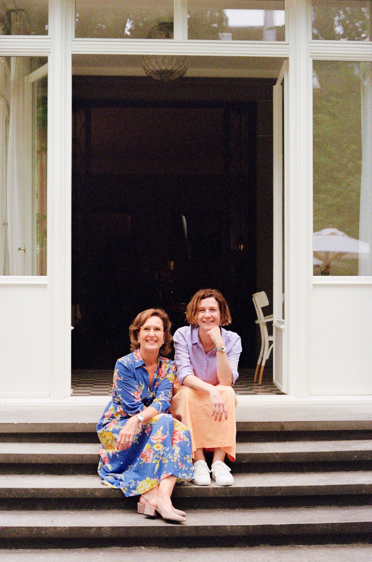 Two women sitting on the steps, one wearing blue and the other in orange - Owners and mangers of Signau House Hotel Zurich | The Art of Desking: Stylish Hotels for Work, Rest & Play – The Aficionados