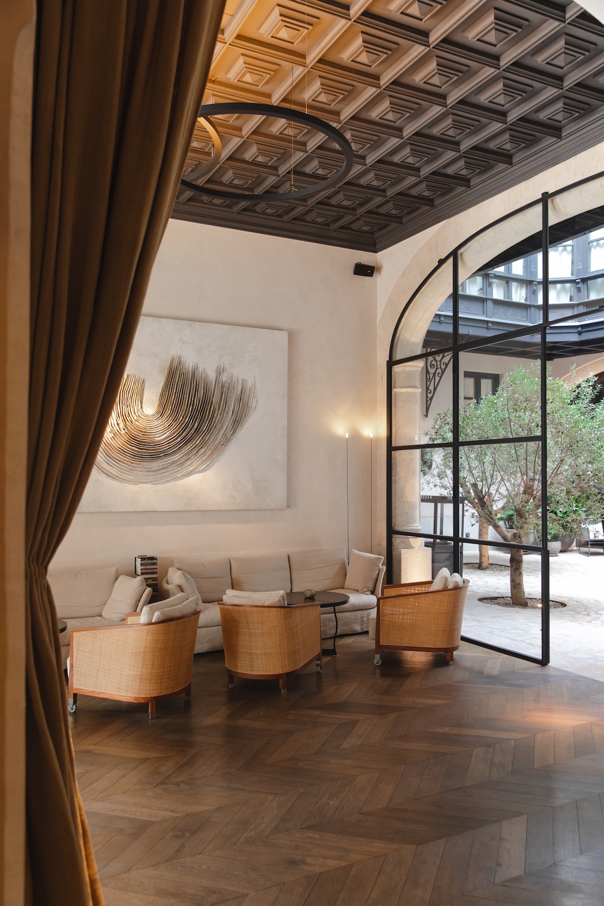 Courtyard lounge at Sant Francesc Hotel with coffered ceiling, cane armchairs and a Crittall arch onto the olive-tree patio | The Aficionados