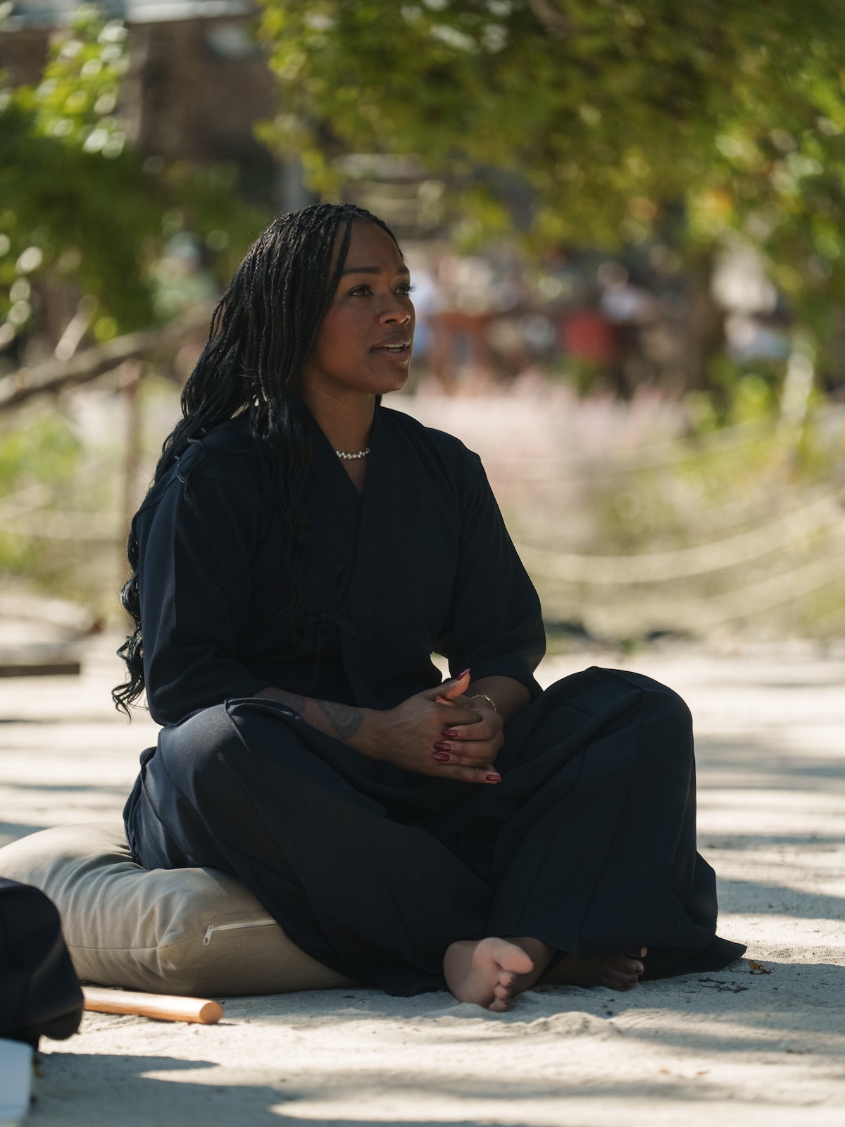 A participant sits cross-legged with hands clasped in calm reflection during a nature-based Zen Samurai meditation session at AHAMA.