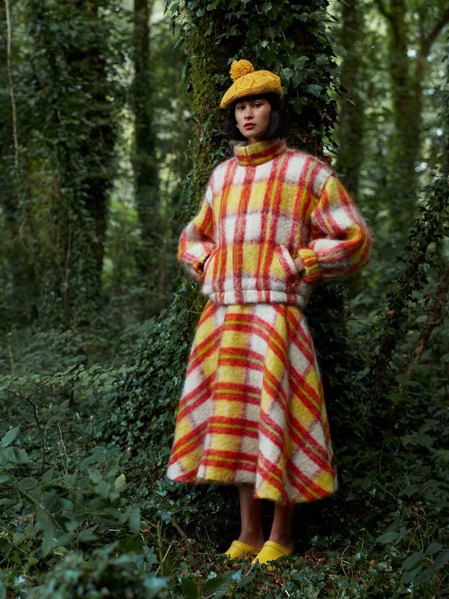 Model in woodland wearing a yellow and red checked mohair jumper and matching full skirt, with a yellow pom-pom beret and yellow mules.