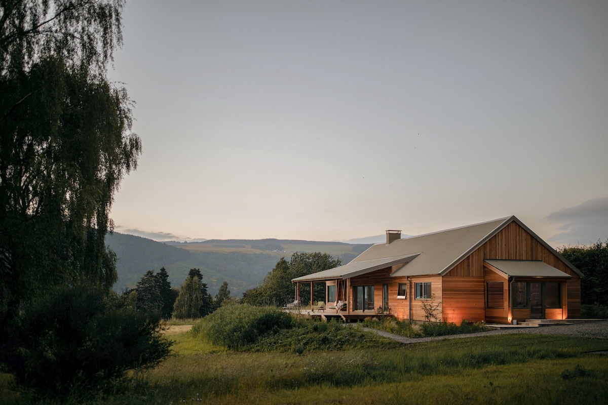 The Lodge at Dun Aluinn at dusk, a cedar-clad timber lodge glowing with warm light above the Tay valley in Highland Perthshire.
