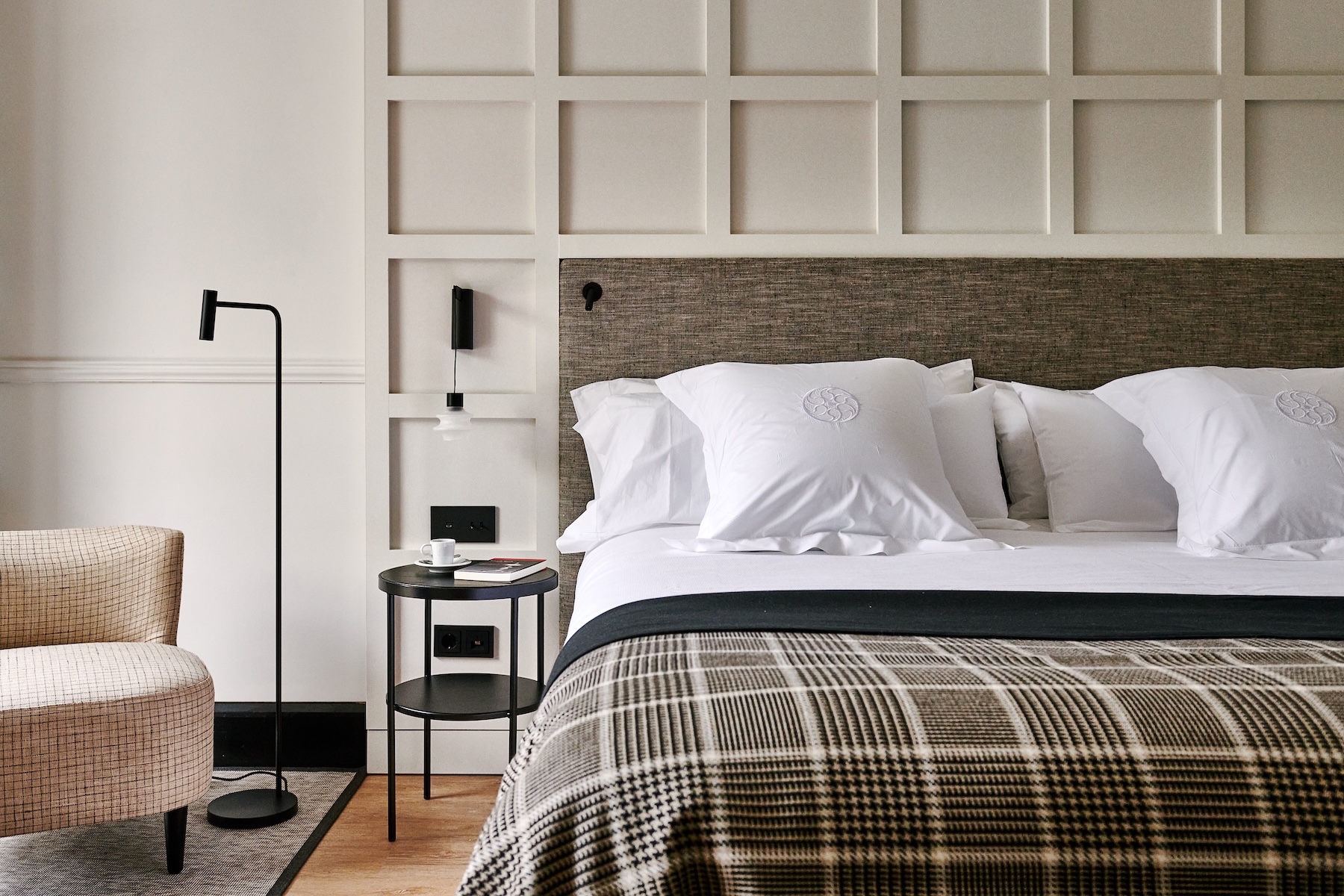 Guest room at Villa Soro with a panelled headboard wall, tweed armchair and Prince of Wales check throw | The Aficionados