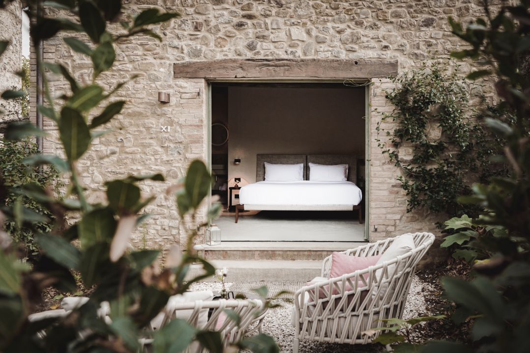 Open window of a luxury desgin hotel bedroom onto patio with rustic stone walls | Vocabolo Moscatelli | The Art of Desking: Stylish Hotels for Work, Rest & Play – The Aficionados