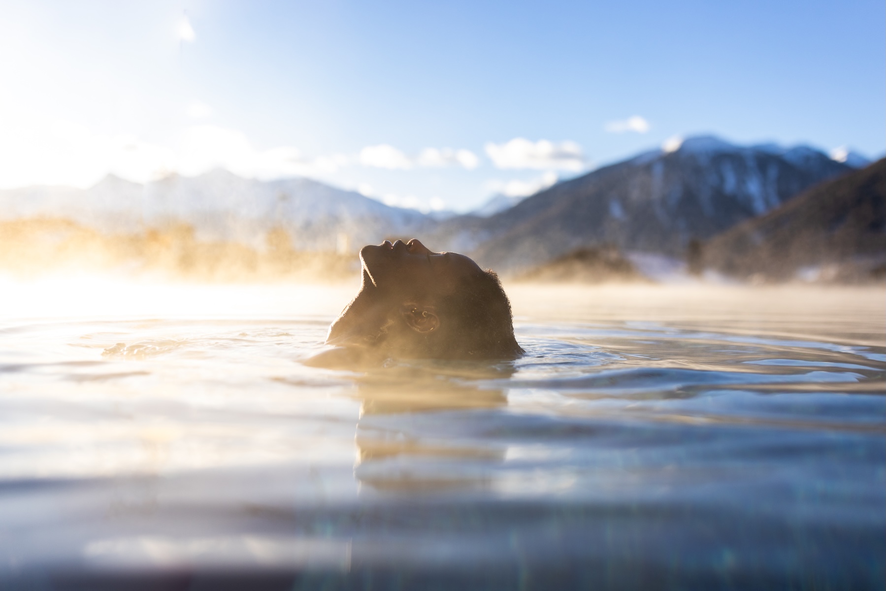 person swimming in an infitiy pool with view of the Alps mountains reflective waters | Aura Mea Spa at Weißes Kreuz | One of the Best Spa Hotels in South Tyrol
