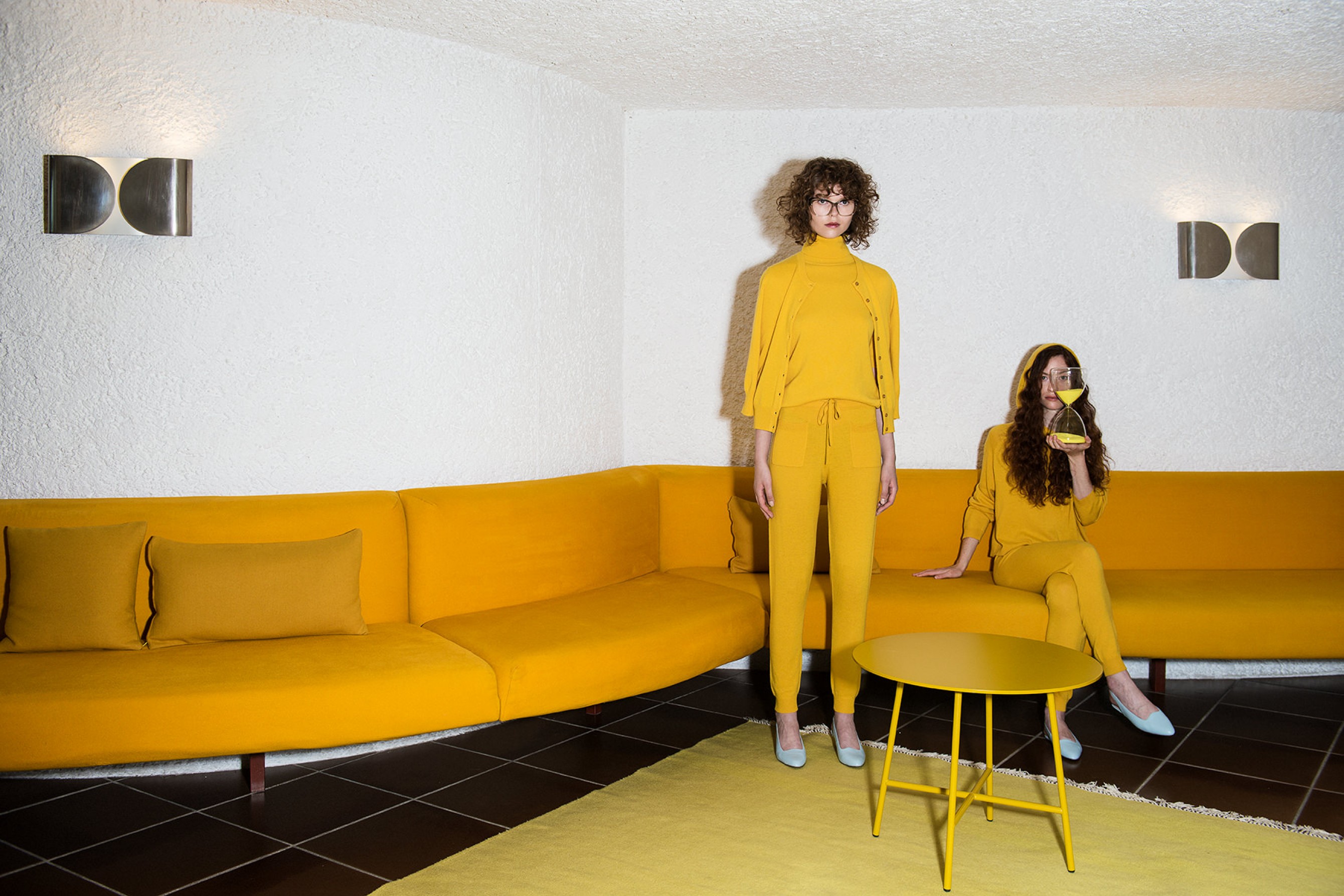 Groovy couple in yellow fashion outfits against a yellow sofa - design 70s hotel Seehotel Ambach Italy | Poetic Design Hotels & Creative Hideaways Across Europe – The Aficionados
