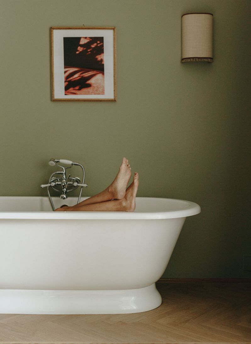 Free standing white bathtub against green wall with thebhint of someone in the bath with their feet poking out| Parkhotel Mondschein | Bolzano, South Tyrol Italy | The Aficionados |South Tyrol Hotels by the Dissertori Brothers | Design & Architecture